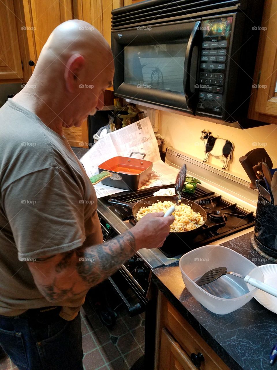 #stayathome - cooking at home. Man cooking at stove making breakfast for family. Scrambled eggs cooking under lighted stove top.