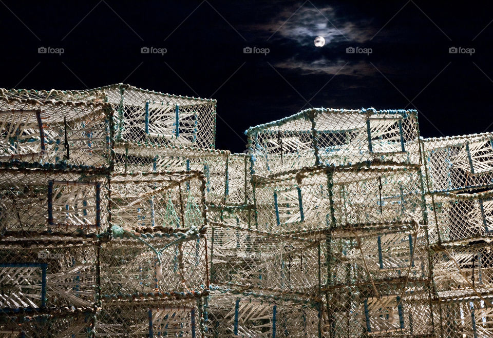 Stacks of lobster pots pictured on a bright night with the moon slightly obscured by clouds