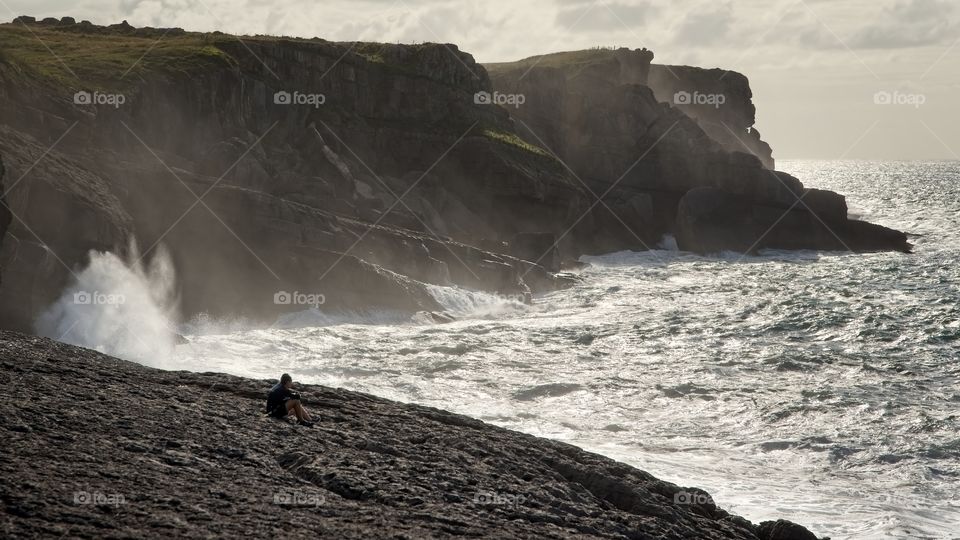 A couple of hikers rest and contemplate the sea as the waves splash next to them
