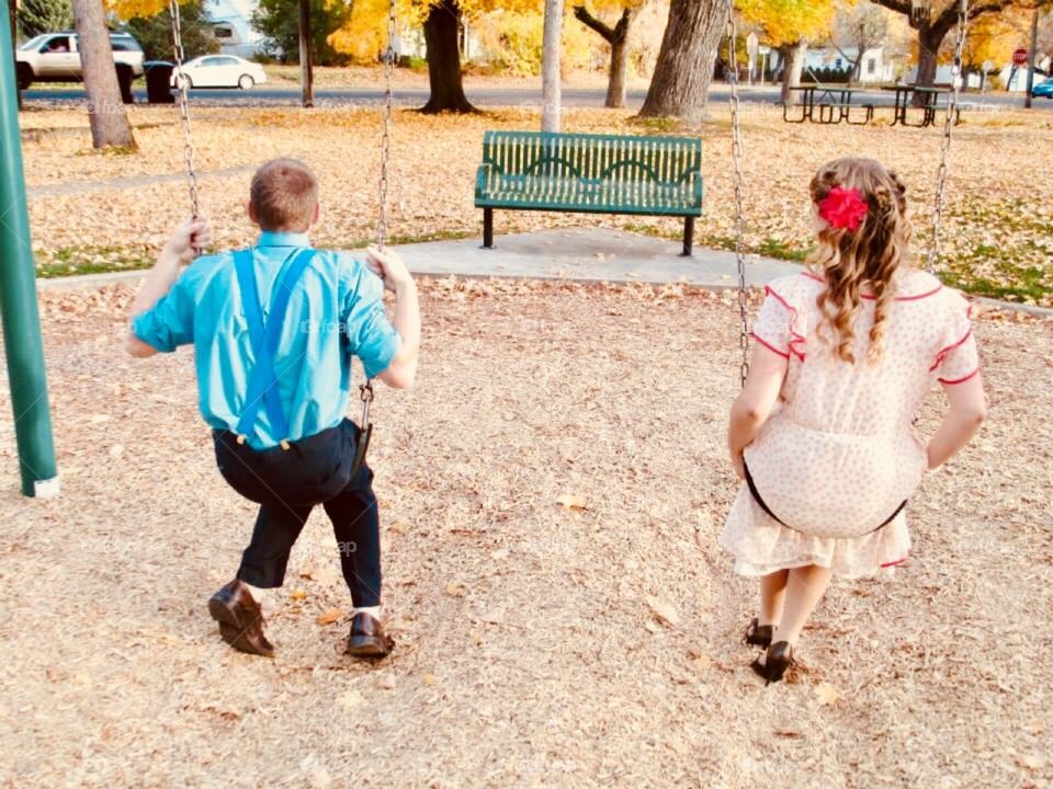 This photo presents a fun look into the past through a Halloween costume get-together. A boy and girl in 1940s fashion spent time enjoying the swings.