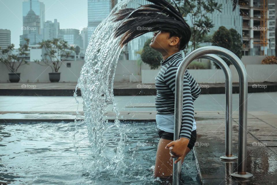 little girl waving her long wet hair at swimming pool.