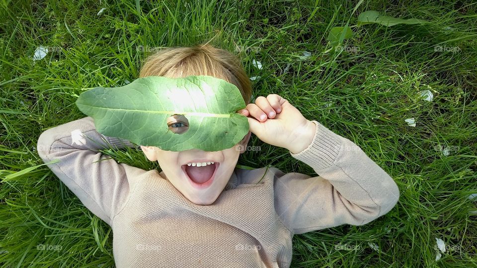 smiling little boy with a leaf on the grass