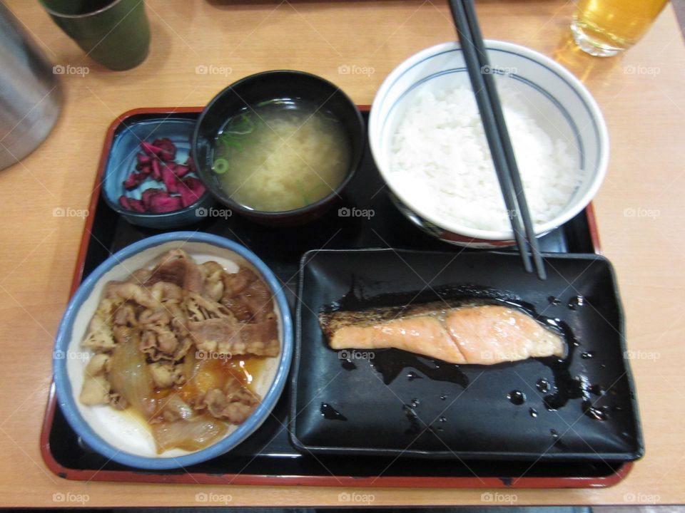 a traditional Japanese lunch set with white rice, fish, miso soup, pickled vegetables and meat dish, served on black and white dishes with chopsticks