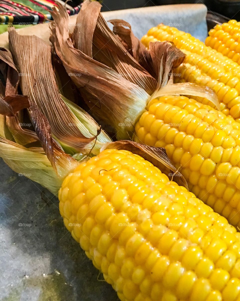 Close-up roasted corn on the cob corncob with husk yellow buttery delicious