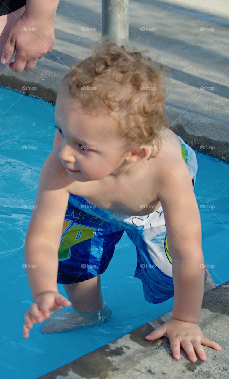 A toddler boy at the outdoor swimming pool for his first round of swimming lessons on a sunny summer evening. 