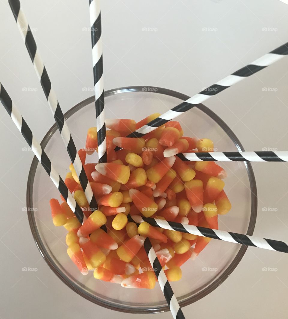 Yellow, orange and white, Colorful Candy corn in a glass bowl with black and white swirly straws. Halloween treats 