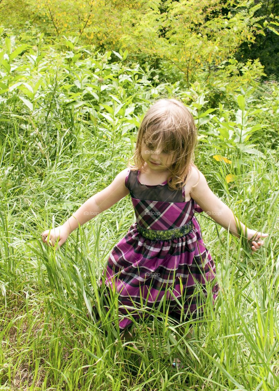 Little girl wearing a purple plaid dress walking through the weeds 