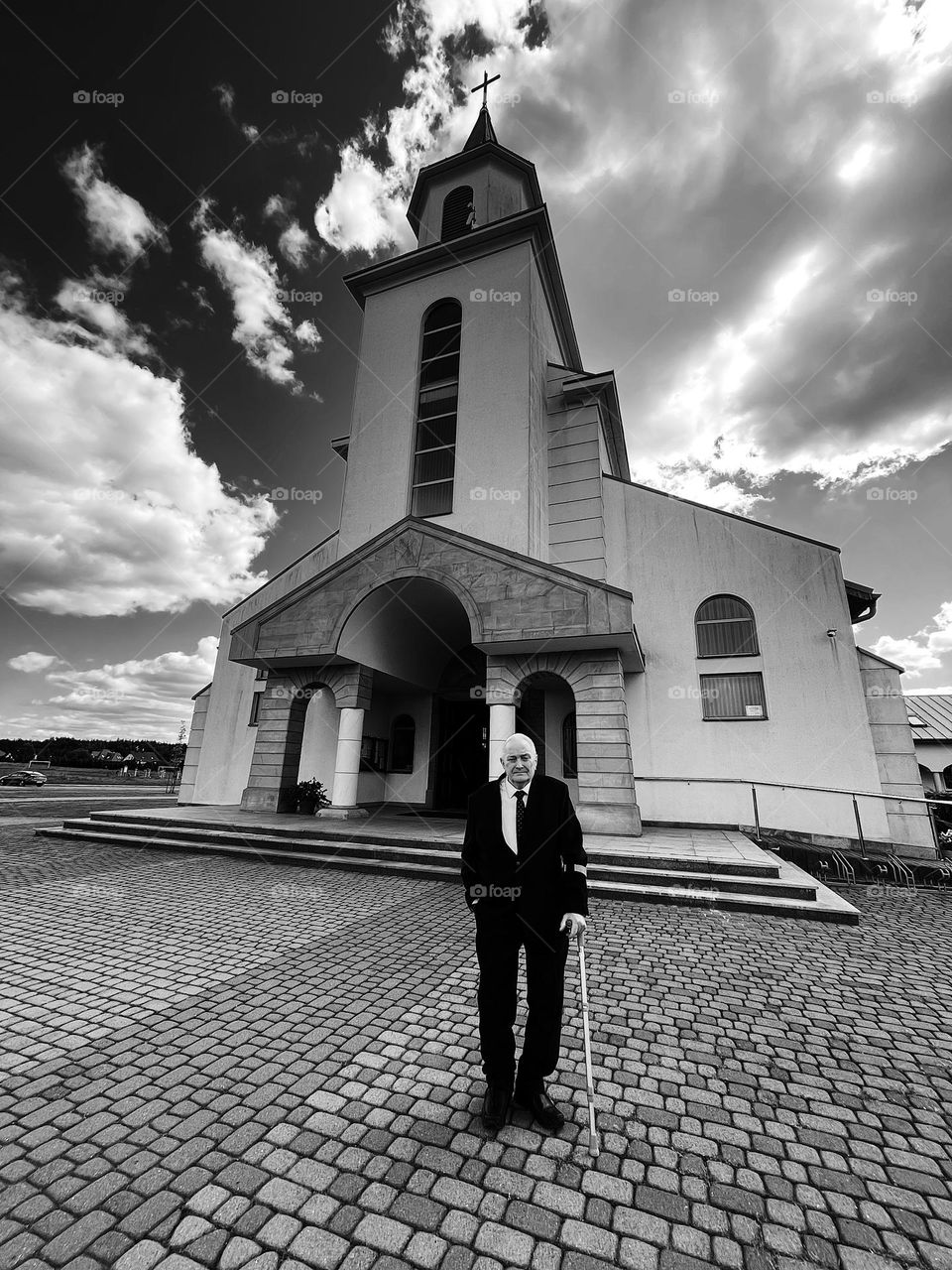An elderly man in a suit with a crutch stands in front of a Catholic church