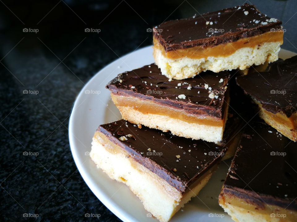 Millionaire's shortbread with chocolate and caramel slices in a white plate on black background.