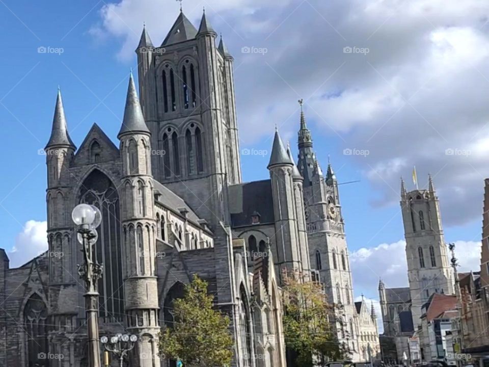 Facade of Saint Nicholas' Church (Sint-Niklaaskerk) with the clock tower of Belfry of Ghent (Het Belfort) and Saint Bavo Cathedral (Sint-Baafskathedraal) at the background, in Ghent, Belgium. Typical picture from Ghent