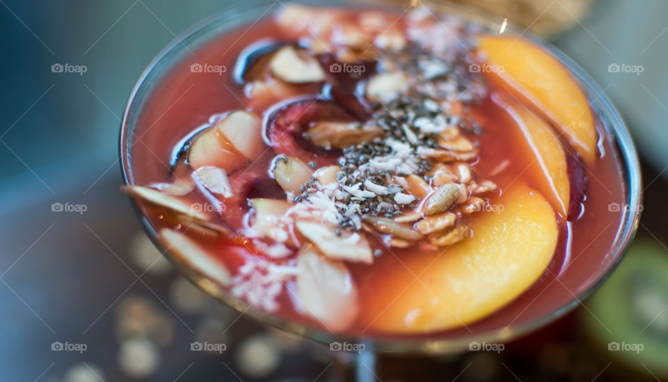 Close-up red fruit smoothly made with berries garnished with oatmeal, chia seed, almond slices, shredded coconut, black cherries, nectarine and fig healthy lifestyle food photography 