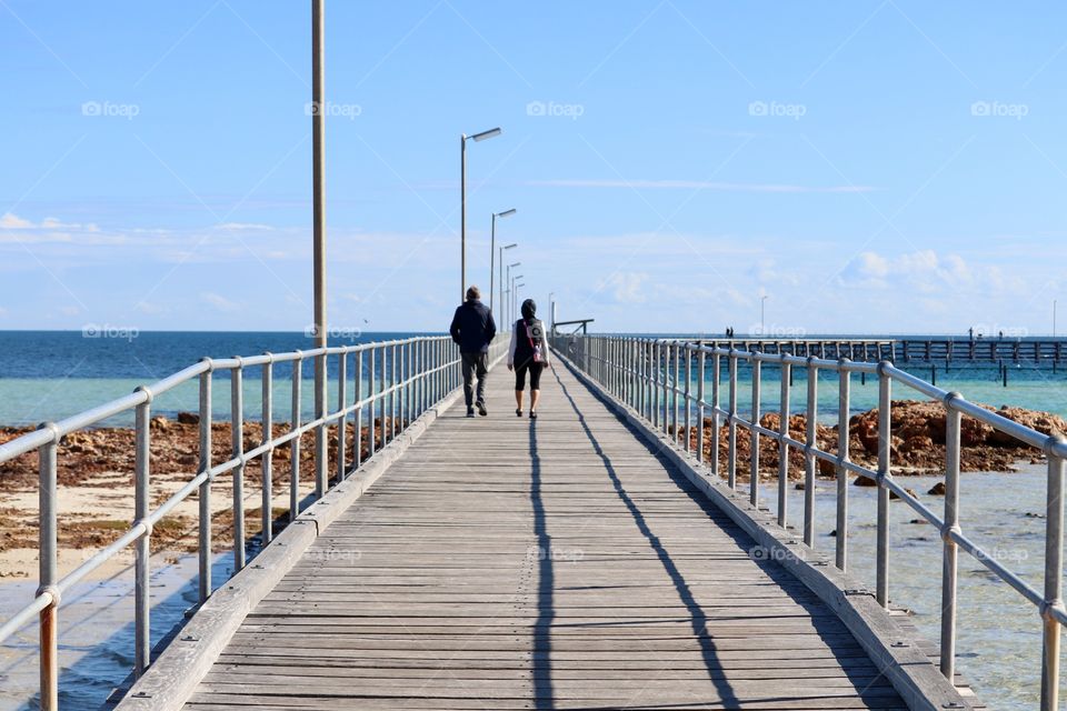 Couple walking away from
Camera down long public wharf Jetty 