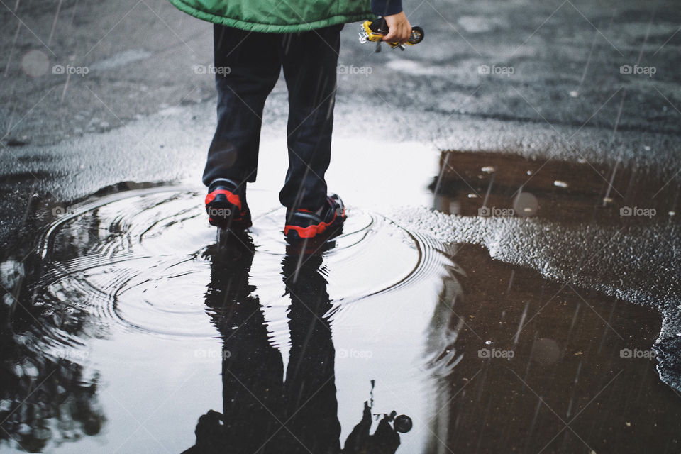 A kid with a toy in his hand walking into a puddle during a rainy day