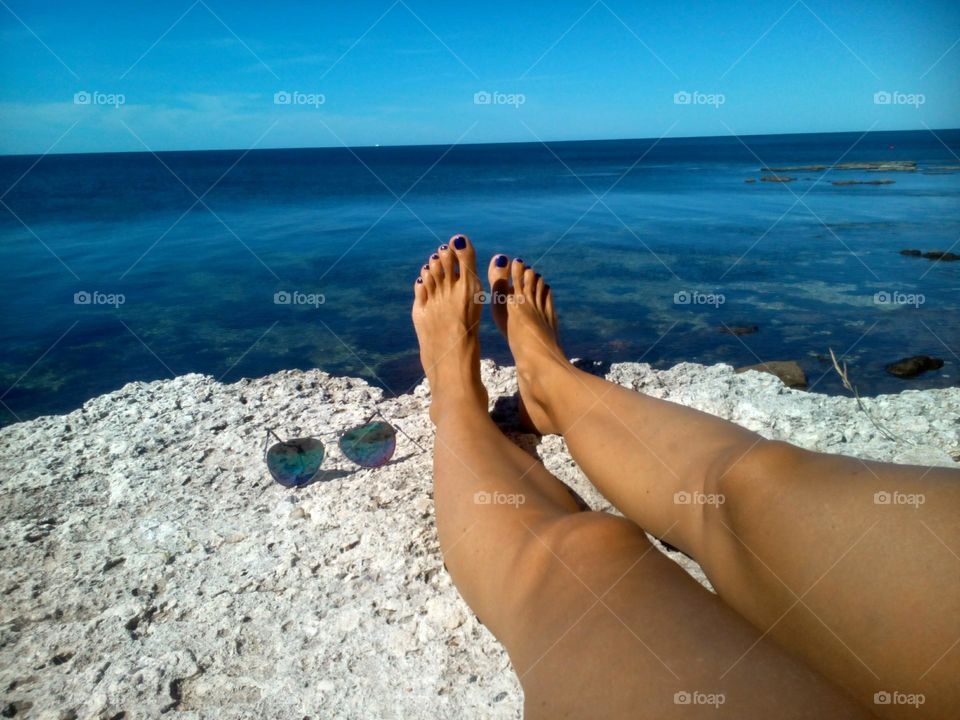 female legs barefoot relaxing on a stone shore view from the ground