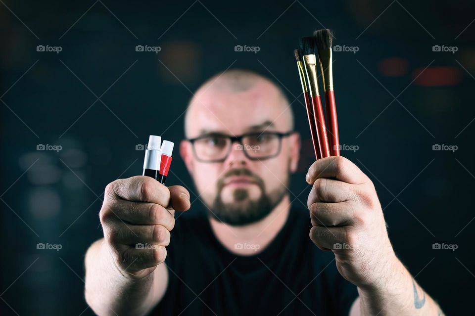 Portrait shot of bearded man holding brushes