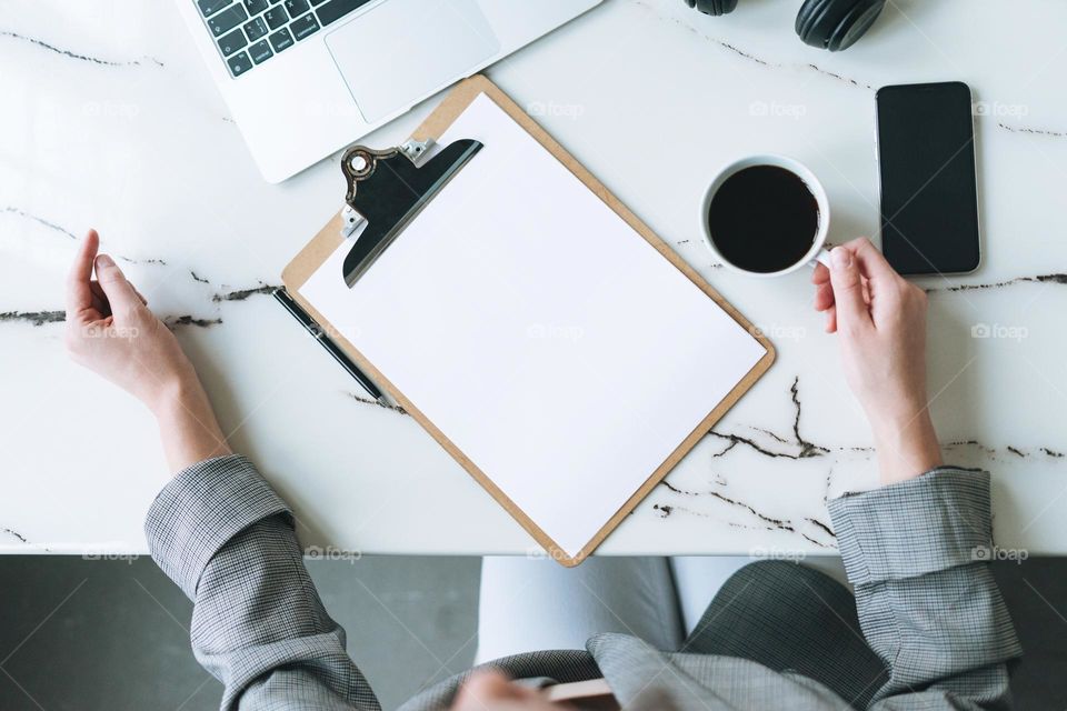 Top view of business woman on working place with cup of coffee, notes, open laptop, smartphone on white marble table in the bright modern office room, mockup