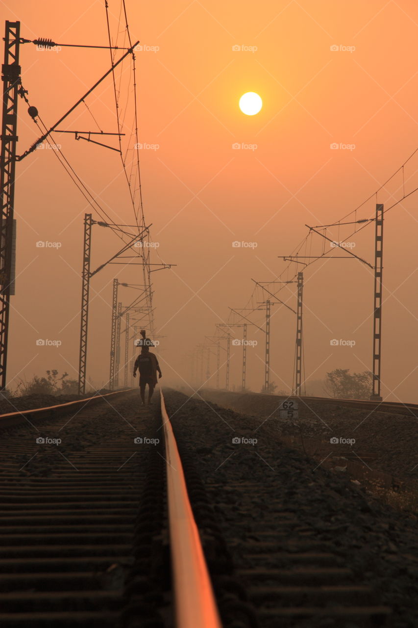 a man with luggage on his head walking alone on a railway track