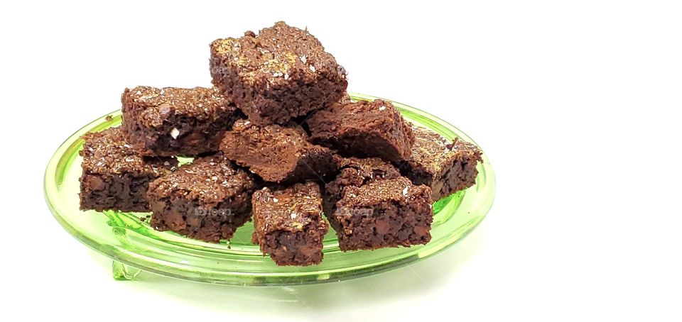 Chocolate brownies on a green glass plate with a white background 
