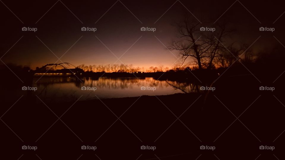 Sunset-Twilight-Night Visible Backlit Skyline. Lake Water Reflections of ShoreLine to Calm Lake Waters. 
