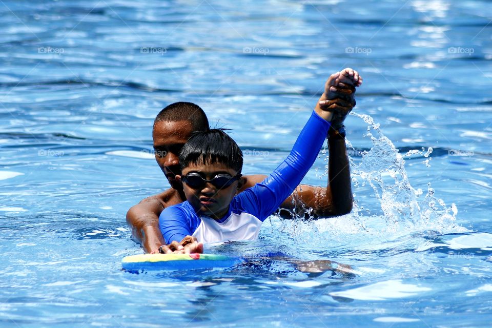 young kid learns how to swim with the help of a swimming coach