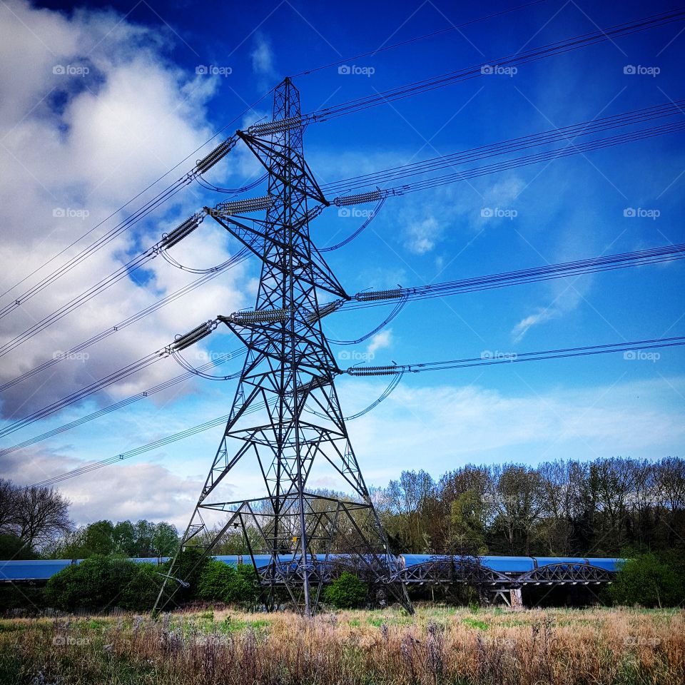 Electricity Pylon in front of BMW Mini train under a blue sky in Oxford, UK