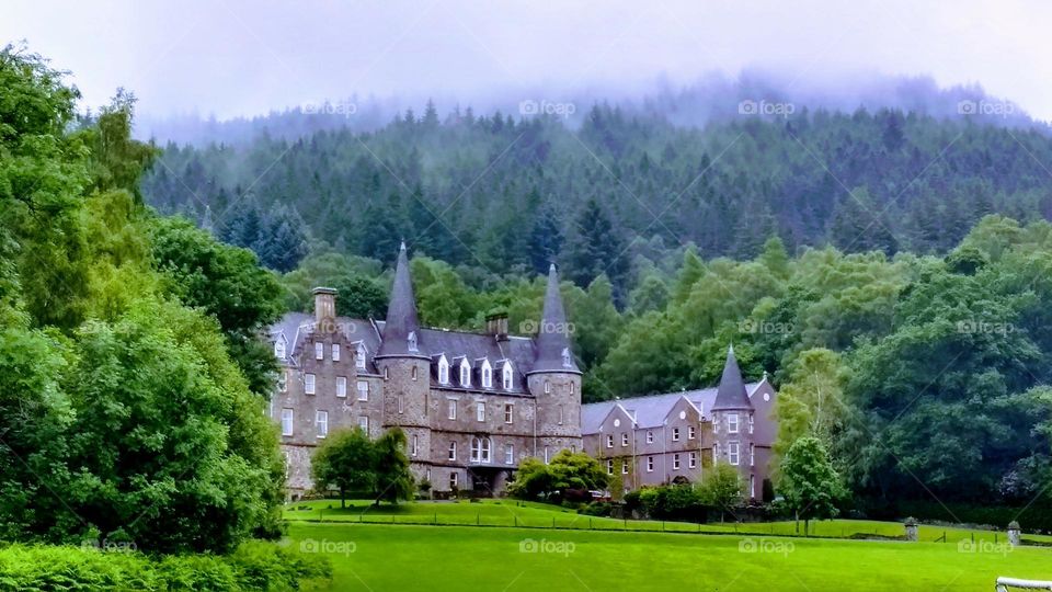 Tigh Mor Trossachs private Victorian turreted castle-hotel in the Trossachs National Park, Scotland with forests and mist in the background and fields in the foreground