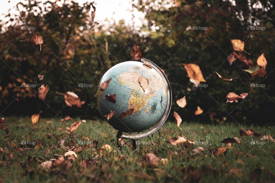 A concept portrait of a world globe surrounded by falling leaves during fall, autumn season.
