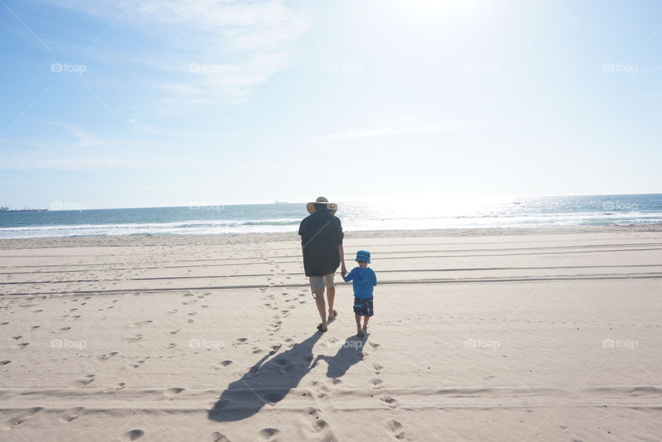 Grandmother and grandson hold hands as they walk toward the ocean
