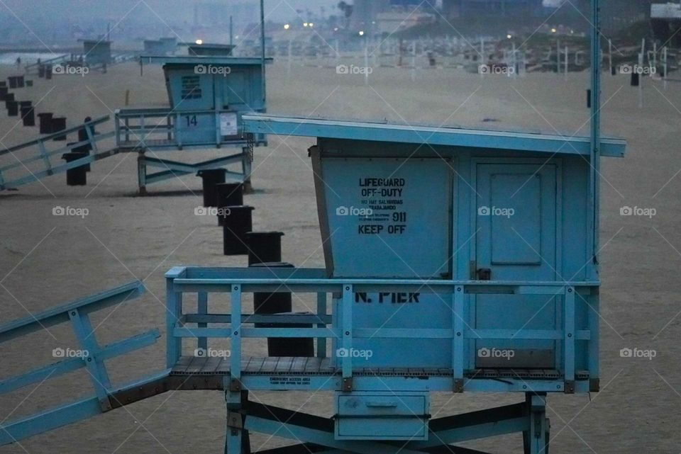 Lifeguard stations and trash cans create a repetitive scene along a beach