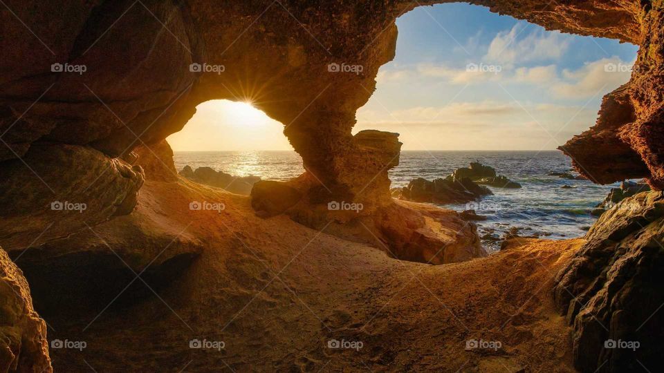 beautiful view of the sun going down to the sea from the entrance of a cave