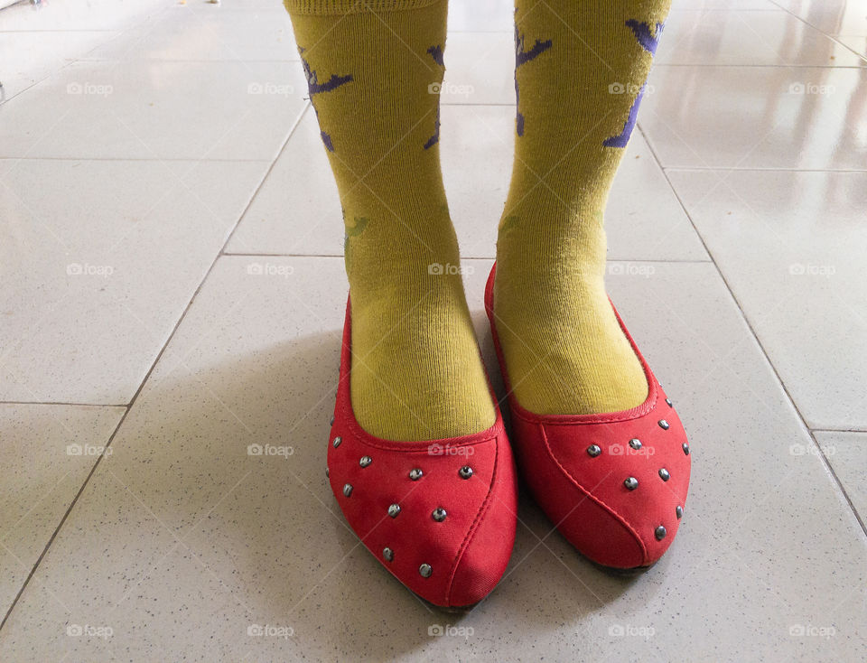 A picture of a lady wearing a red footwear and a yellow socks standing on a tiled floor with legs showing.