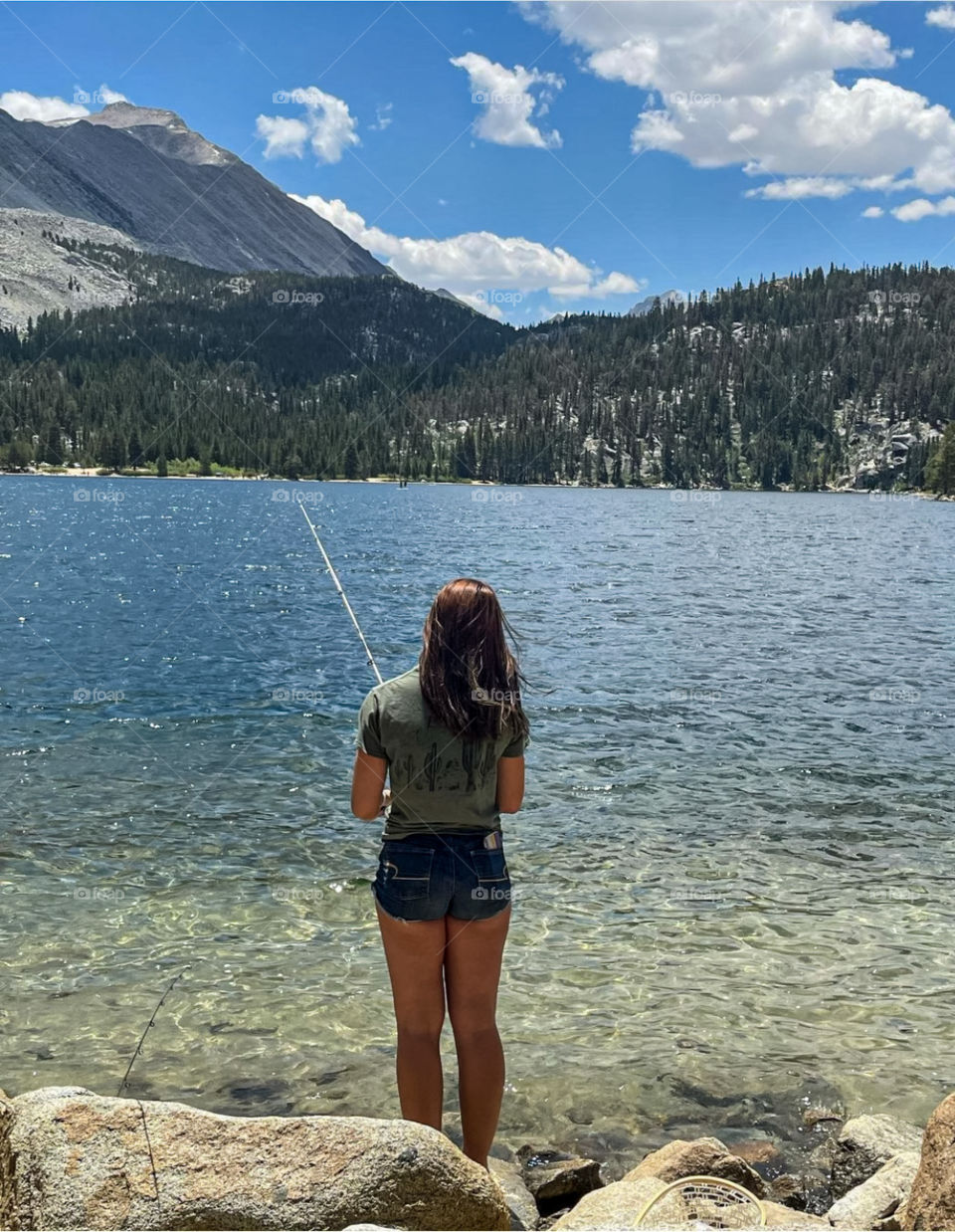 A girl fishing in a sparkling mountain lake on a summer day. 