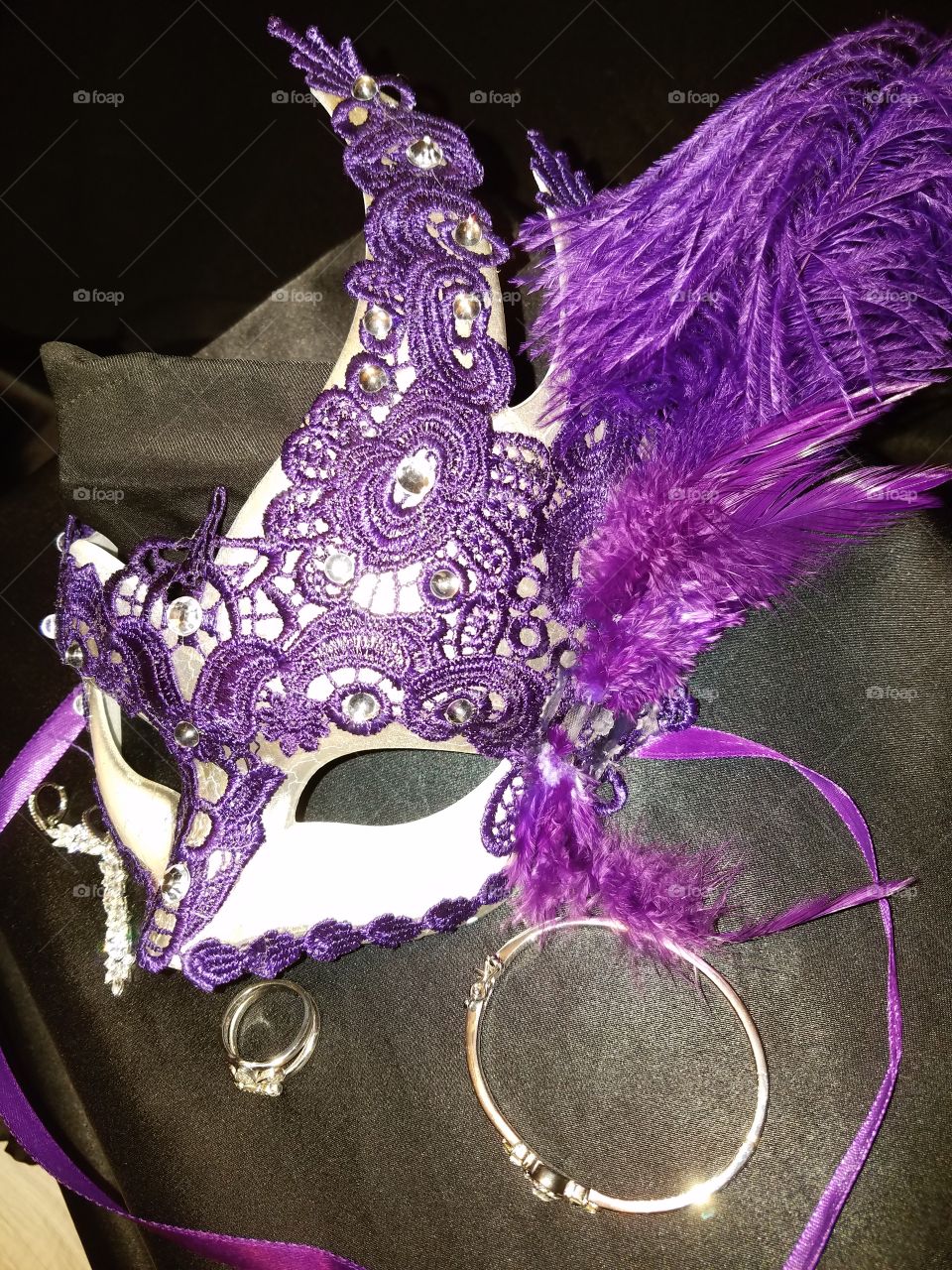 purple lace white mask with purple feathers purple satin ribbons. Diamond Jewelry earrings ,Florida Lou ring and bracelet on a satin black background.