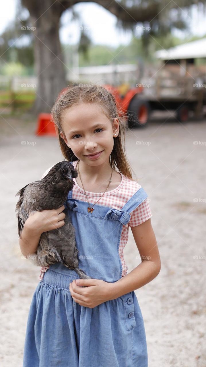 Young country girl  holding a chicken  with one hand