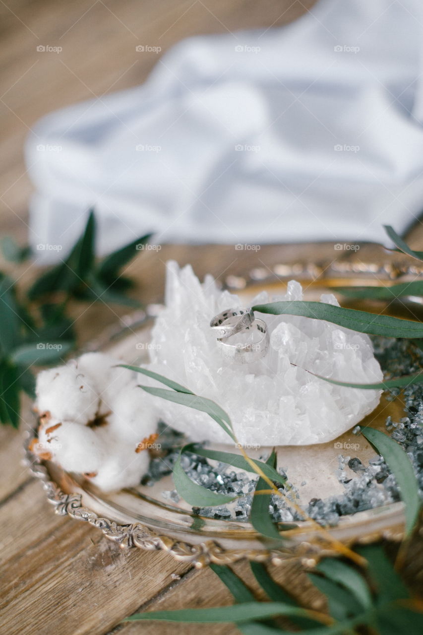 Silver plate with two wedding ring and white crystal on wood background.