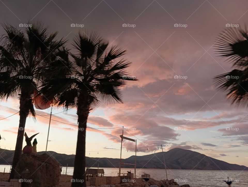 Silhouettes of palm trees against the sunset sky and mountains