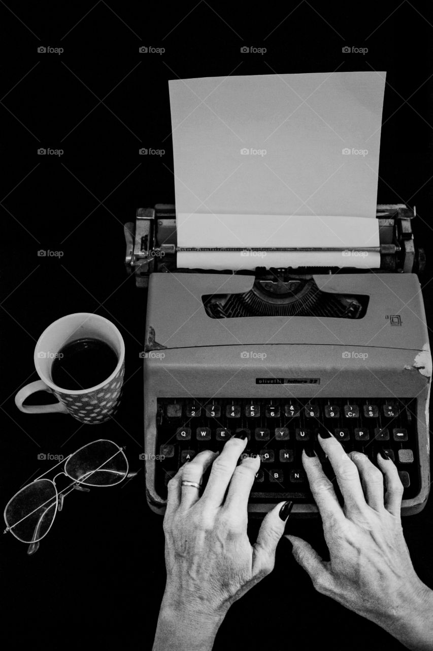 Woman typing on the old typewriter with a cup of coffee
