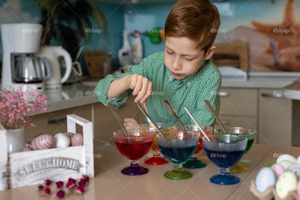 Easter traditions. Red-haired boy paints eggs in the kitchen