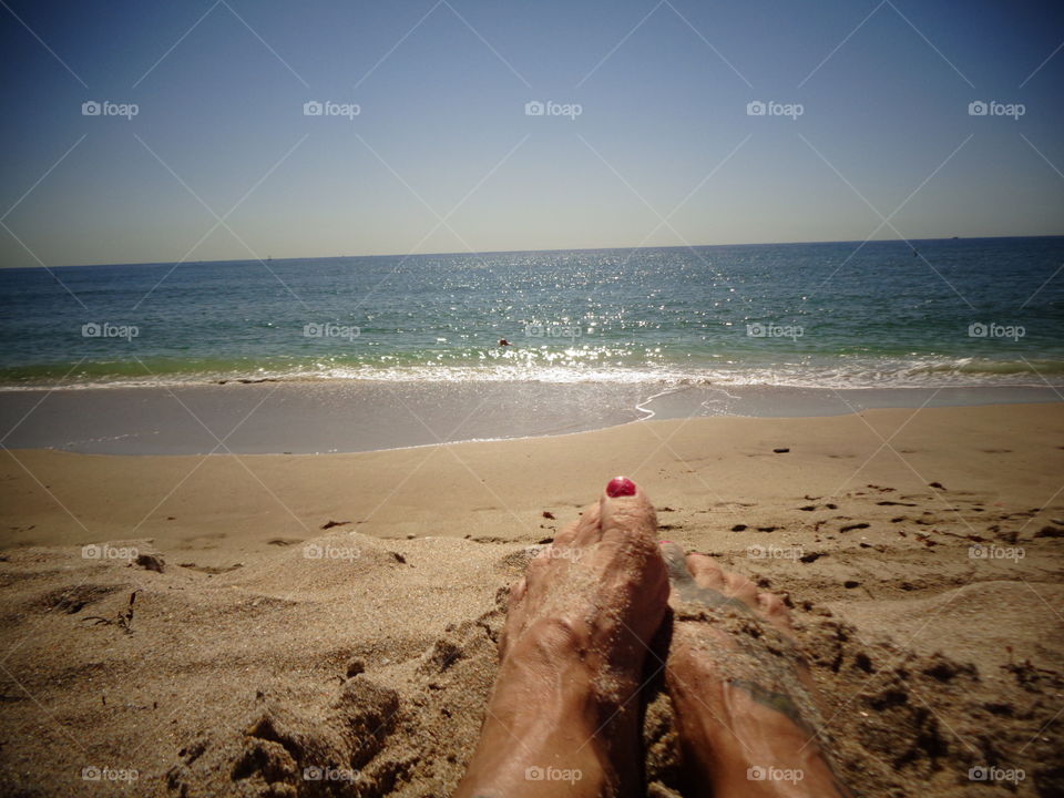 Bare feet with painted toenails alone near the surf.