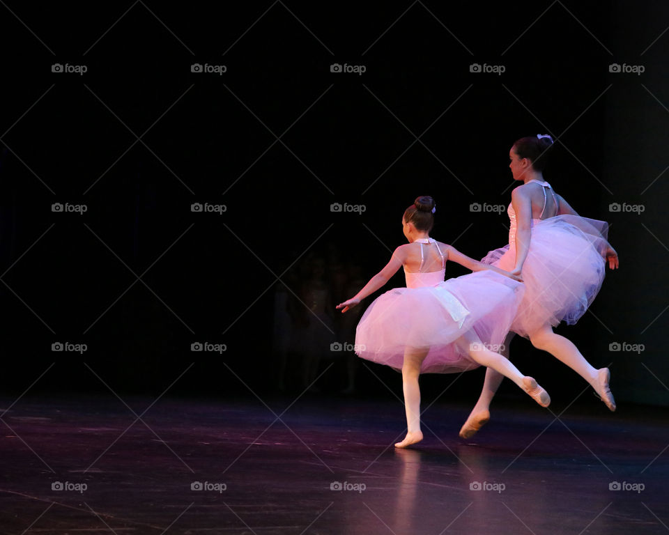 Two young ballerina’s in pink tutus dance across the theatre stage
