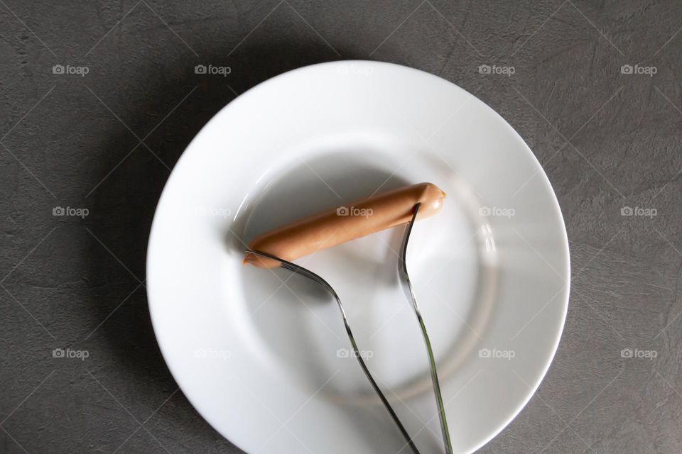 One fork is pierced with one hot dog during times of famine and lack of food with sunlight and shadows.