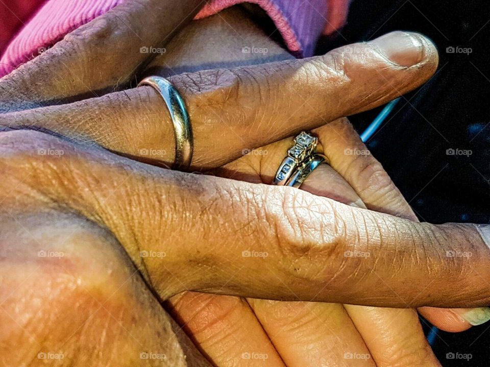 Older Hispanic and Caucasian couple hands only together clasped wearing wedding rings 