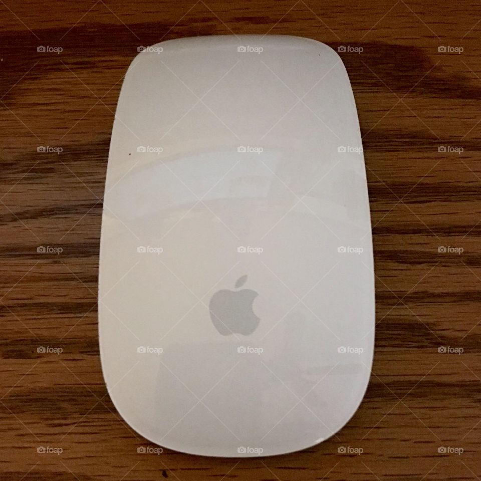 Wireless Apple mouse on wood grain surface.