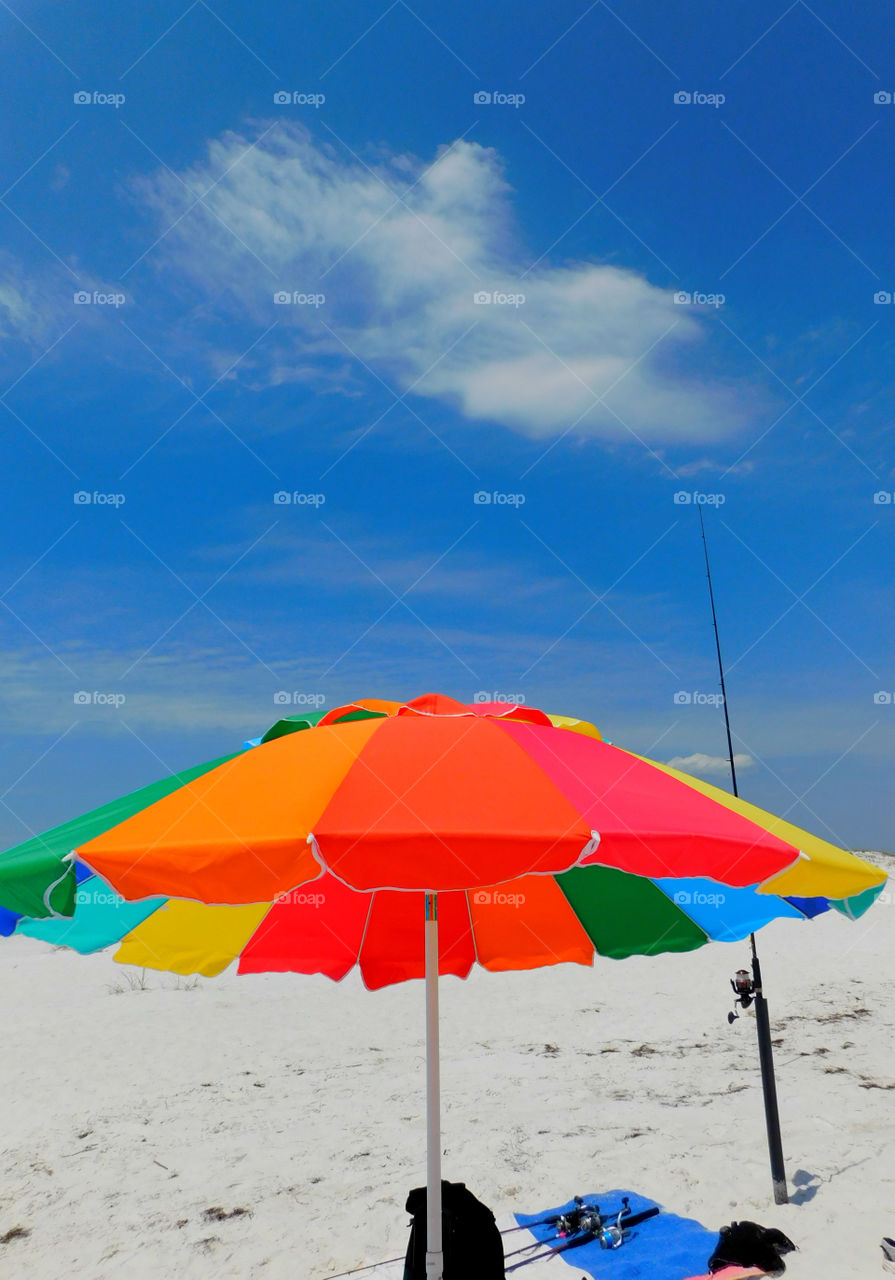 I love these colors - Foap Missions - A brightly colored umbrella stands in the white sand of the Gulf of Mexico with a bright blue sky backdrop 