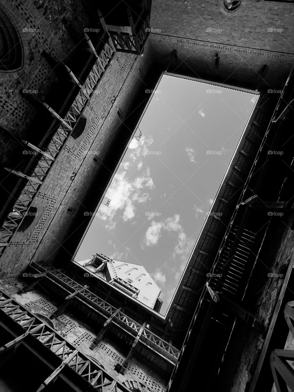 Look up into a cloudy sky framed by the open roof of the castle building.