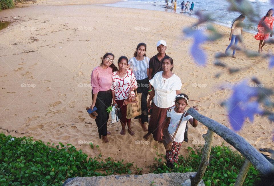 This is a family enjoining their leisure time in the sea beach. There are two women, three girls and on boy wearing a cap.They seems very funny and spending happily their leisure time with together .ππ