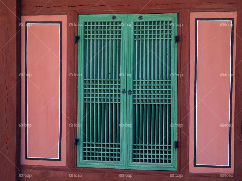 A closeup of a colorful green window surrounded by pink shutters at the reconstructed Royal Gyeongbokgung Palace complex in Seoul, South Korea.