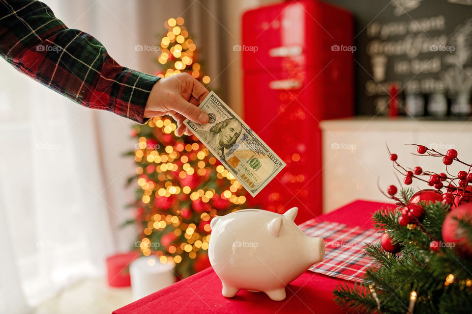 piggy bank with 100 dollars banknote in festive New Year atmosphere of scenery.  Magical bokeh with Christmas tree and bright lights.