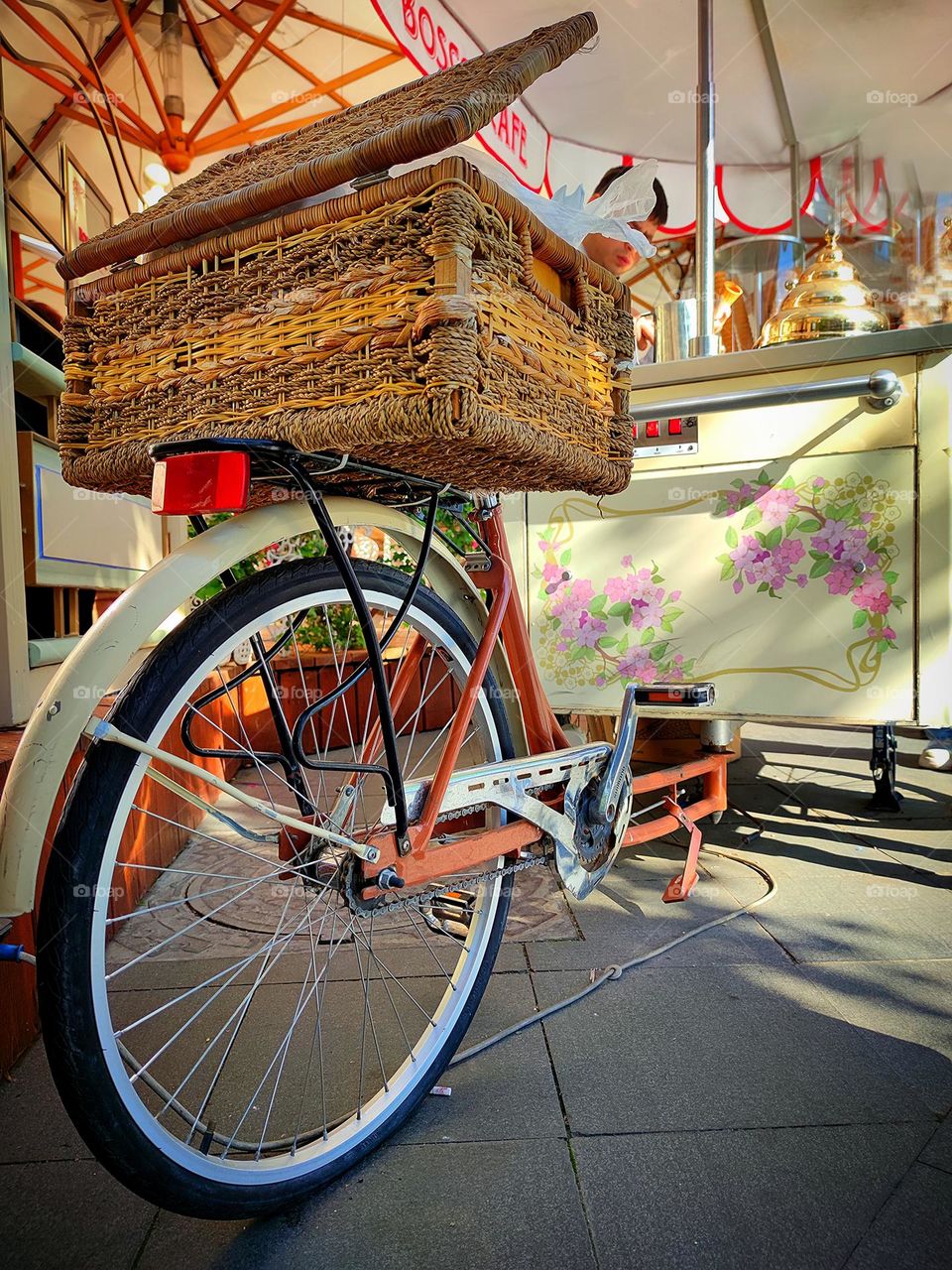 Bicycles.  the back of the wheel that will connect to the ice cream freezer.  A wicker basket is attached to the seat of a bicycle.