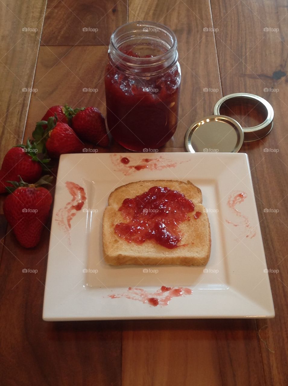 Homemade strawberry jam in a jar with a slice of toast.